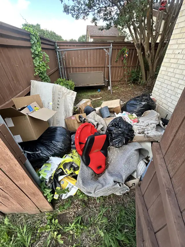 Fenced side yard filled with bags, boxes and junk before cleanup